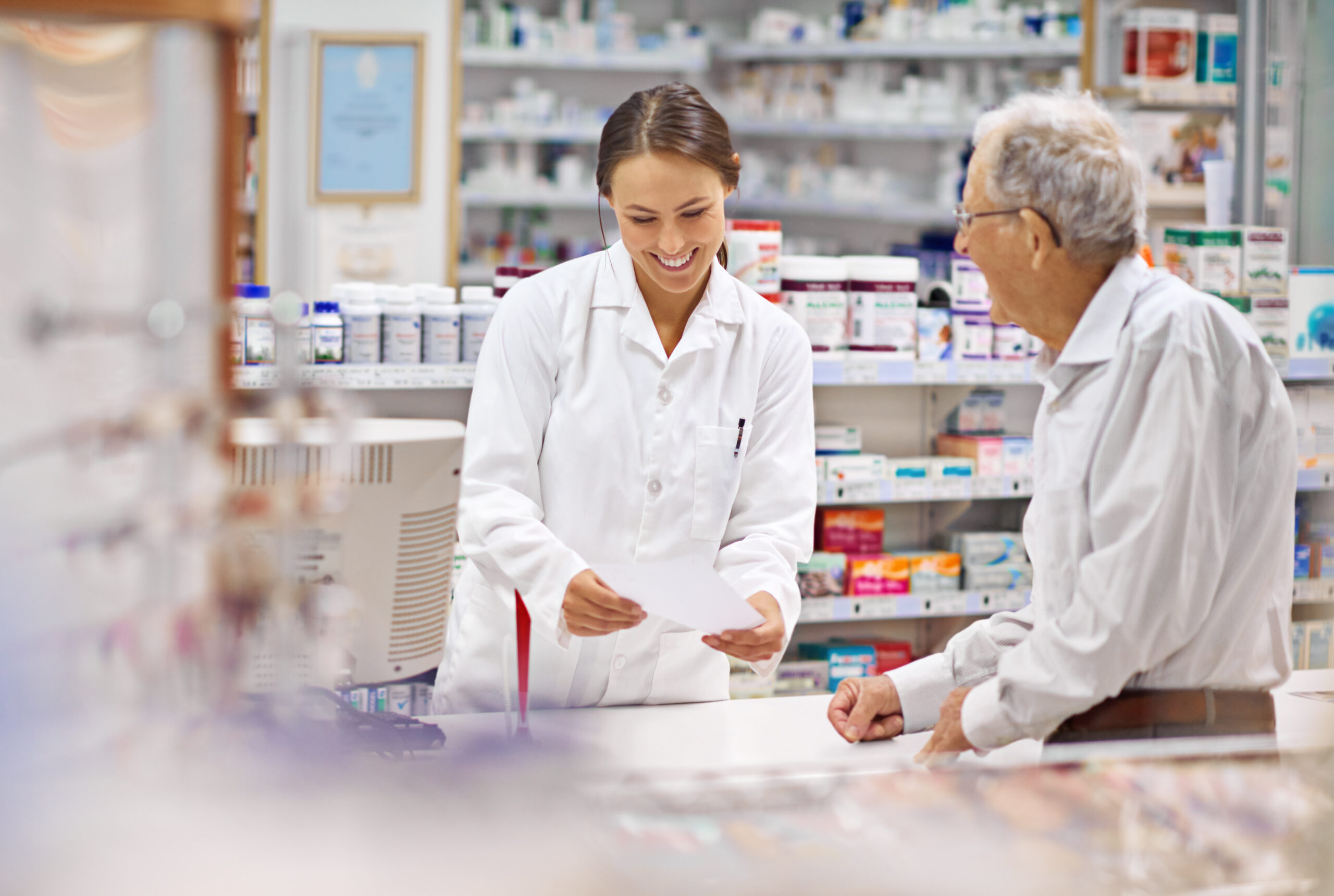 Smiling pharmacist holding prescription in front of man at pharmacy